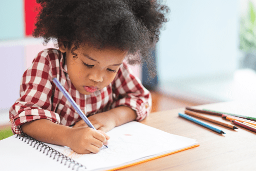 Young student writes in a notebook at their desk.